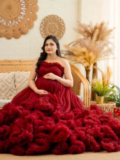 A full shot of the mom-to-be seated in our boho studio, the red gown creating a stunning visual centerpiece.
