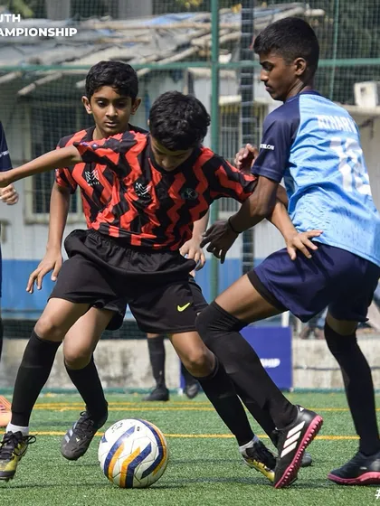Surrounded but not beaten. Our young player skillfully protects the ball from two opponents, showcasing great composure under pressure.