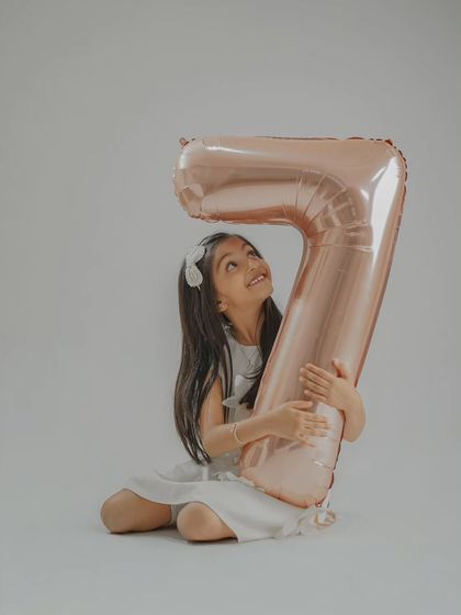 The birthday girl hugging a giant number '7' balloon. Using large props like this adds a fun and personal element to milestone birthday photos.