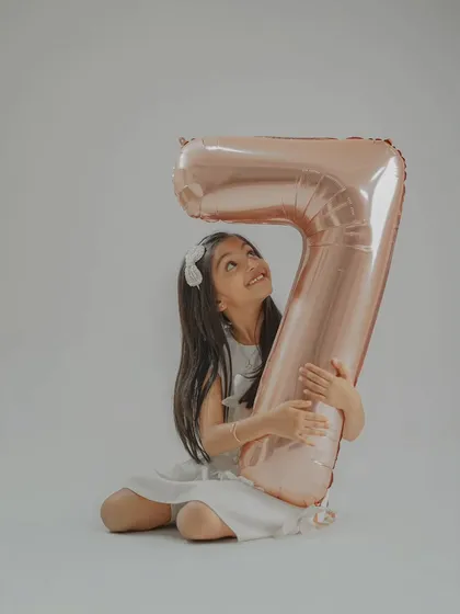 The birthday girl hugging a giant number '7' balloon. Using large props like this adds a fun and personal element to milestone birthday photos.
