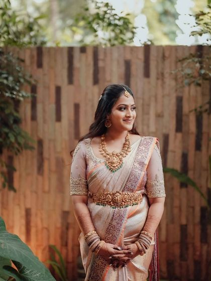 A bride in a soft pastel saree with a delicate embroidered border. The sheer sleeves of her blouse are adorned with matching embroidery, creating a look of ethereal beauty.