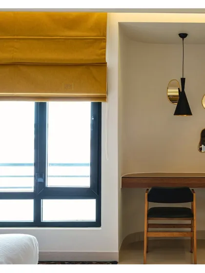 A detail of the study nook in a guest room, featuring a simple wooden desk and organically shaped mirrors. The mustard-yellow roman blinds add a pop of color and warmth.