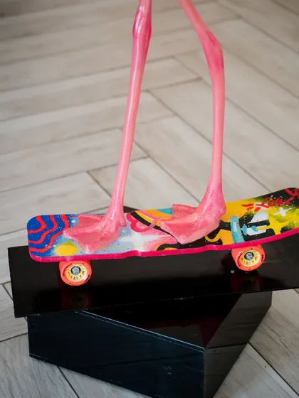 A detail of the pop-art skateboard beneath the flamingo, its colorful design a stark contrast to the bird's natural grace.
