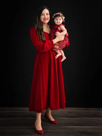 A graceful mother and daughter portrait. The mother stands tall, holding her daughter, both in beautiful red dresses, creating an image of pure elegance.
