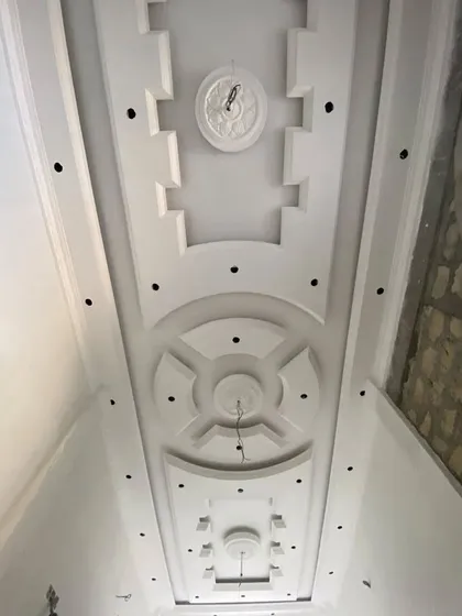 A long and ornate ceiling for a hallway, shown after the POP work is complete but before painting. You can see the various medallions and patterns.