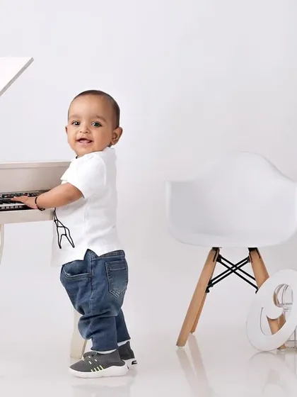 A little boy dressed as a mini-musician, standing and playing at a small white piano in a clean, modern studio setup.