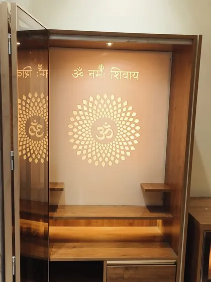 A close-up of the mandir with its doors open, revealing the 'Om Namah Shivay' mantra and beautiful backlighting. The design includes small shelves for idols and drawers for storing pooja essentials.