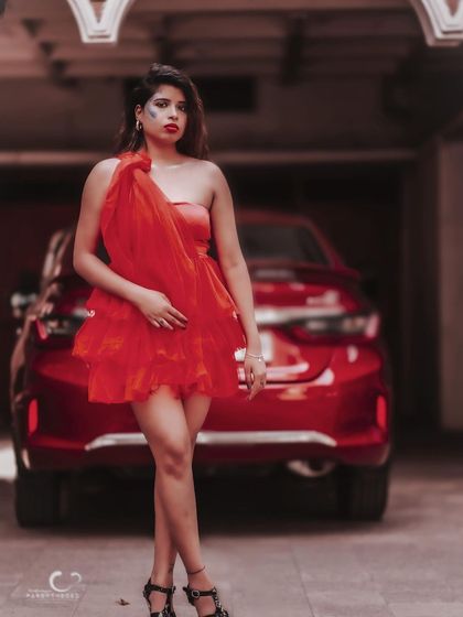 A bold and confident pose in a red tulle dress, set against the backdrop of a red car. The monochromatic color scheme is striking.