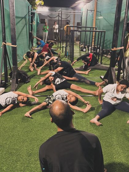 The coach leads the group in a synchronized wide-legged forward fold. This view shows the community aspect of our training, where everyone moves and progresses together.
