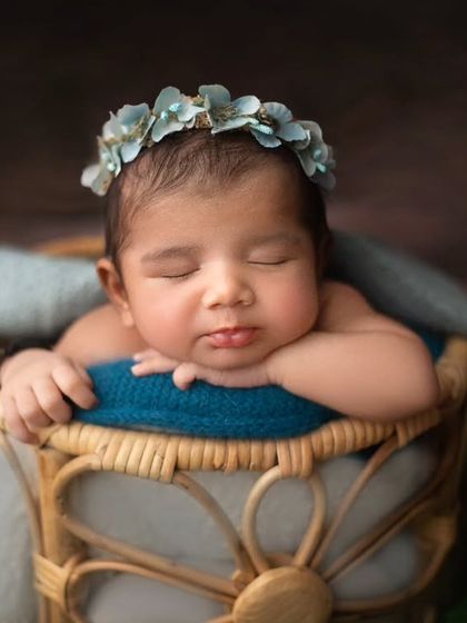 A beautiful combination of textures and colors. The baby rests peacefully in a basket, adorned with a floral crown that complements the blue and green tones.