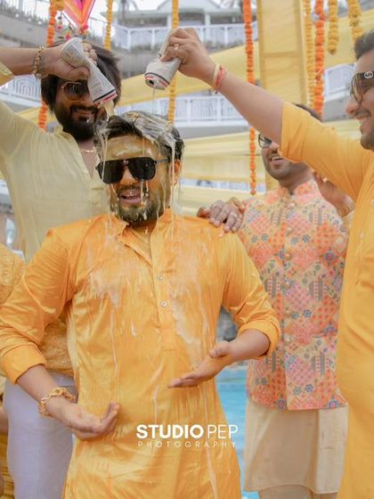 The groom, Nikhil, gets playfully doused with milk and turmeric by his friends, a classic Haldi moment full of laughter and camaraderie.