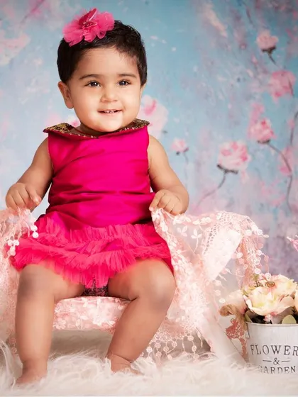 Dressed in a vibrant pink dress against a beautiful floral backdrop, this little girl's smile lights up the entire photo. These sessions are all about capturing the pure joy of being a baby.