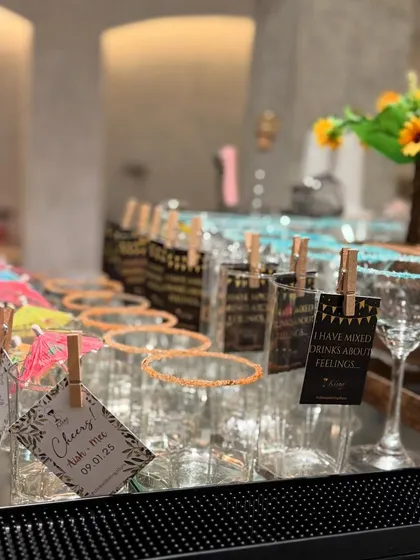 A bar top filled with glasses, each with a unique tag or garnish, from fun quotes to colorful umbrellas, creating a festive and inviting scene.