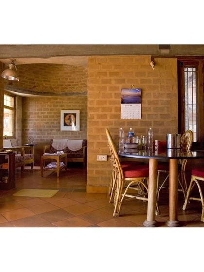 The dining and living area of the Professor's Residence, showcasing the warmth of exposed earth block walls and terracotta floor tiles. The furniture was custom-designed to meet the specific needs and heights of the client.