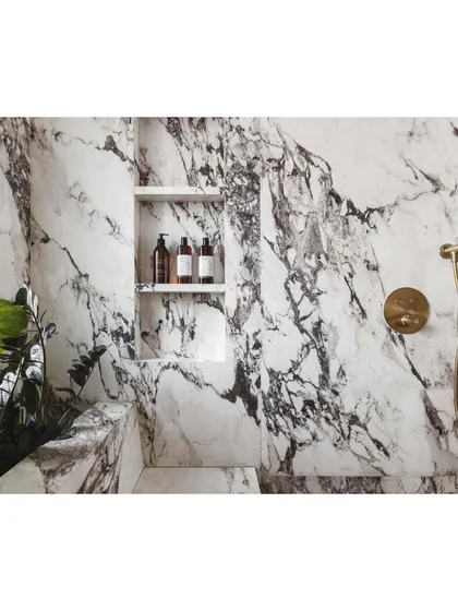 A detail of the shower niche, carved directly into the marble-patterned wall, with elegant brass fixtures adding a touch of warmth.