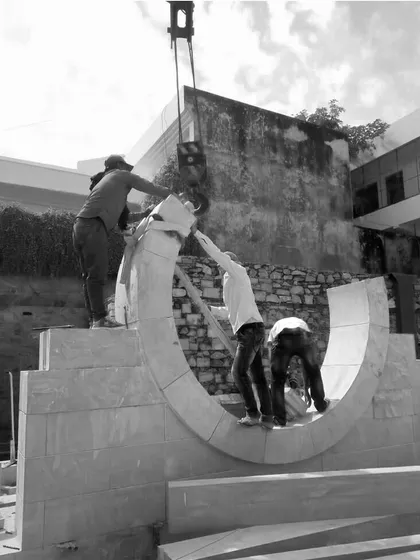 Craftsmanship in action. Workers assemble a curved stone element for the House of Solid Stone, showcasing the skill needed to shape and fit heavy, unforgiving material into an elegant architectural form.