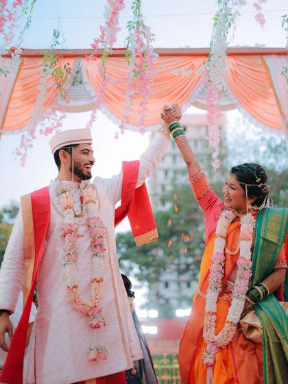 A moment of pure celebration. The couple raises their hands in joy after completing their wedding rituals, with flower petals showering down on them.