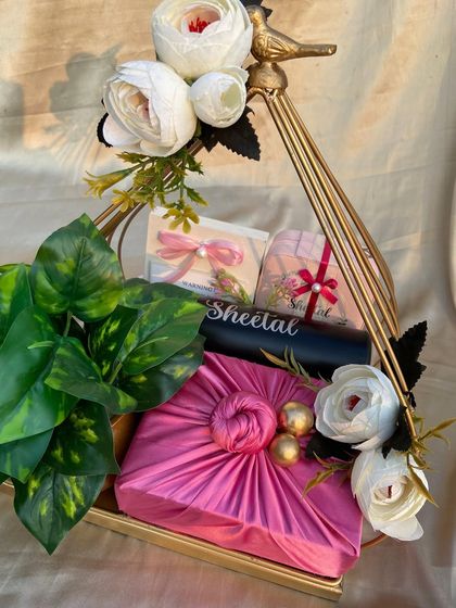 A heartfelt goodbye hamper for a senior. This gift features a Furoshiki-wrapped present, a personalized jewelry organizer, and white flowers, all arranged in a golden metal basket.