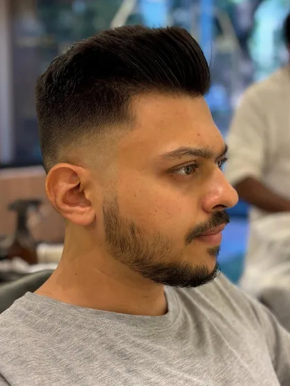 A side profile of a classic men's pompadour with a high fade. The look is sharp, clean, and effortlessly stylish.
