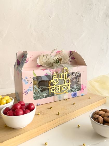 Our floral pink Diwali gift box, filled with treats and accompanied by bowls of panned nuts and almonds, showcasing a complete festive offering.