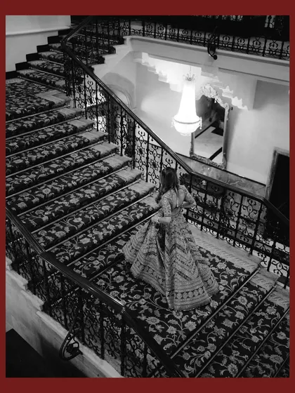 A dramatic black and white shot of the bride descending the iconic staircase of the Taj Mahal Palace. The high angle and architectural details create a grand and timeless image.