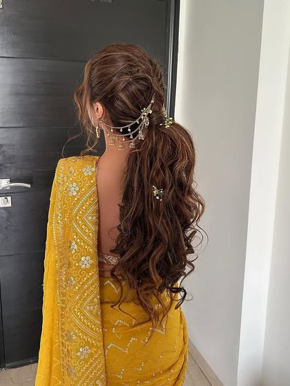 Morning rituals for a Haldi ceremony. This textured ponytail with cascading curls is accessorized with a traditional passa, blending modern style with ethnic charm.