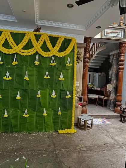 A traditional backdrop made entirely of fresh banana leaves and decorated with yellow flower garlands, perfect for poojas and traditional events at home.