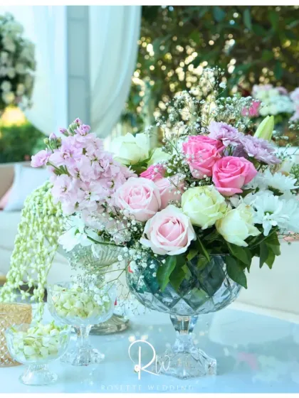 A delicate arrangement of pink and white roses in a crystal compote dish, perfect for a coffee table or lounge area. The addition of fresh jasmine buds in smaller bowls adds a fragrant touch.