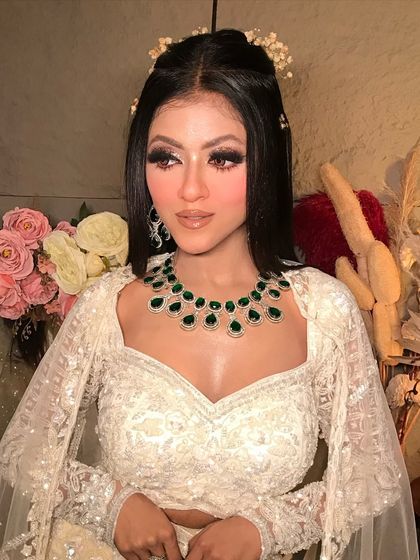 A close-up of the glam evening look. The focus is on the dramatic winged eyeliner, flawless skin, and the stunning contrast of the emerald green jewelry.