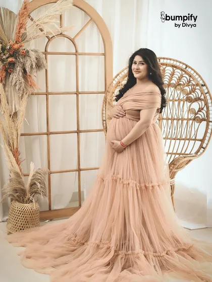 A serene solo portrait of an expecting mother in a beautiful peach gown, seated on a boho-style wicker chair. This shot is all about capturing that quiet, powerful glow of motherhood.