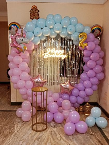 A unicorn theme for a second birthday, featuring a circular balloon arch in pastel pink, purple, and blue. The decor includes unicorn foil balloons and a silver shimmer curtain.
