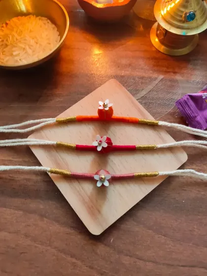 These delicate floral rakhis are handmade with thread and small beads. They come in a variety of warm colors like orange, pink, and red.
