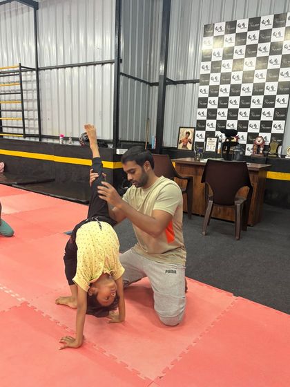 A coach assists a young boy with his backbend walkover, providing support to build flexibility and strength.