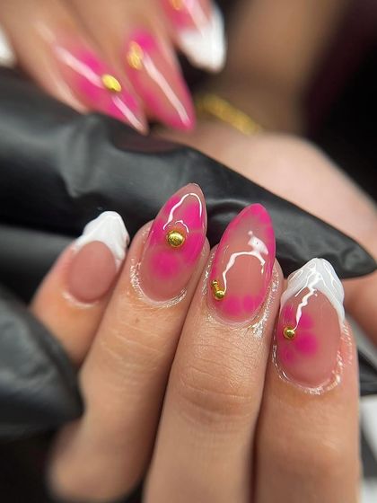 A close-up of a pink watercolor or 'jelly' nail with gold stud accents. This technique creates a beautiful, translucent effect.