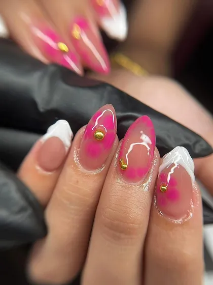 A close-up of a pink watercolor or 'jelly' nail with gold stud accents. This technique creates a beautiful, translucent effect.