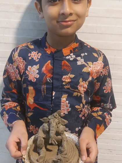 A young boy proudly holds his handcrafted Ganesha idol. Our workshops are designed to build confidence and give children a sense of ownership over their festive creations.