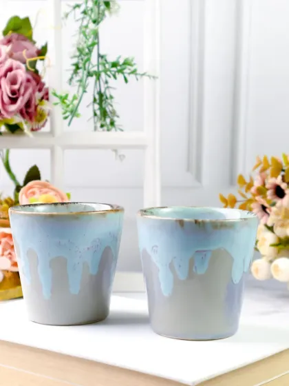 Two ceramic tumblers are styled on a book with a bright, floral window scene in the background. This creates a lovely, light-filled image that feels like a peaceful morning.