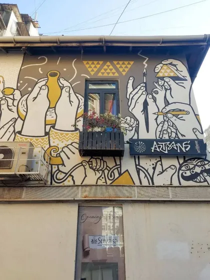 The exterior of the Artisans' gallery in Kala Ghoda, featuring a mural of many hands engaged in creative acts like painting and sculpting. The art perfectly reflects the purpose of the building.
