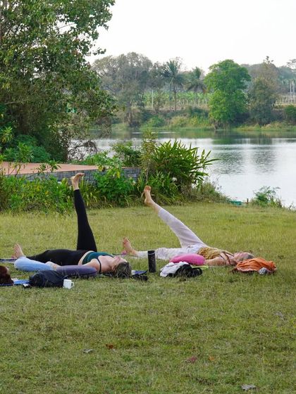 Students practice Yoga Nidra on the grass by the river. This guided relaxation technique is a powerful tool for deep rest and integration, which we teach as part of our comprehensive curriculum.