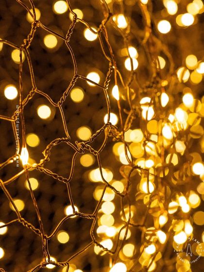 A close-up of the 'Clouds of Abundance' light, focusing on the beautiful bokeh effect created by the numerous small LEDs. The golden wire mesh adds warmth and texture to the overall design.