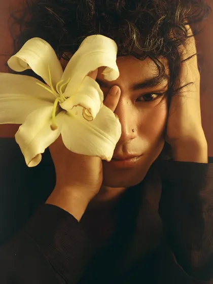 A soft, intimate portrait from a series exploring masculinity and vulnerability. The lily flower held close to the face adds a gentle, poetic element to the image.