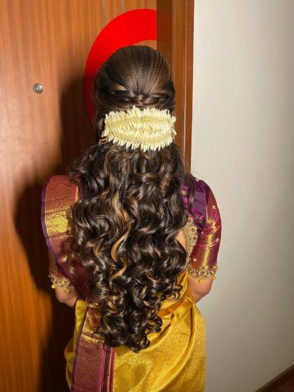 An engagement look with a braided half-updo and voluminous curls, finished with a traditional jasmine gajra.
