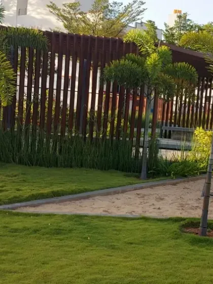 A children's play area with a sandpit and climbing frame, set within a lawned area and bordered by modern fencing. I design safe and fun landscapes for all ages.