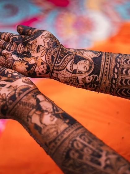 A creative shot showing the bride's full mehendi design against a vibrant orange background. The composition is modern and eye-catching.