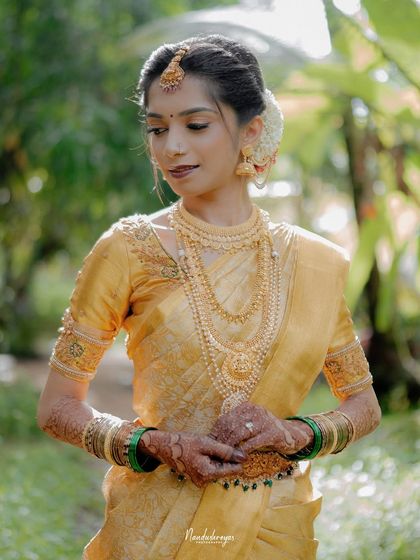 A stunning portrait of the bride in her golden-yellow silk saree. The soft, natural light highlights her traditional jewelry and graceful posture.