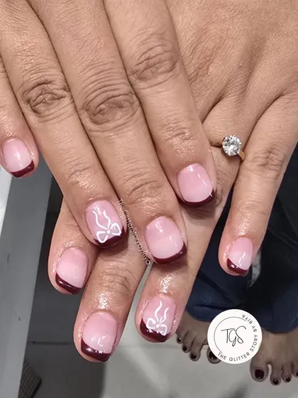 A simple yet festive holiday design. This set features a classic French manicure with deep red tips and delicate, hand-painted white bows on the accent nails.