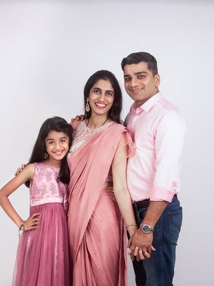 A classic family-of-three portrait in the studio. The coordinated pink outfits and simple white background result in a clean, elegant, and timeless image.