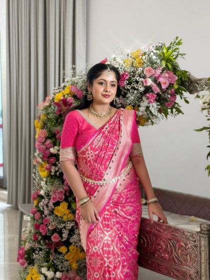 This client looks lovely in a bright pink patterned saree, paired with a matching blouse that has a simple embroidered border on the sleeves.