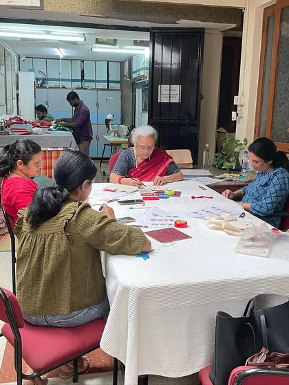 A full view of a mirror work workshop. The table is a hub of activity as students learn to stitch shimmering mirrors onto fabric.