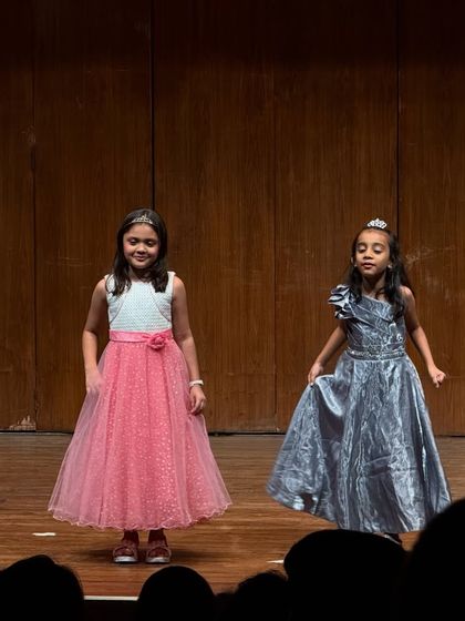 Two friends perform a duet, their coordinated dresses and joyful expressions showing their great chemistry.